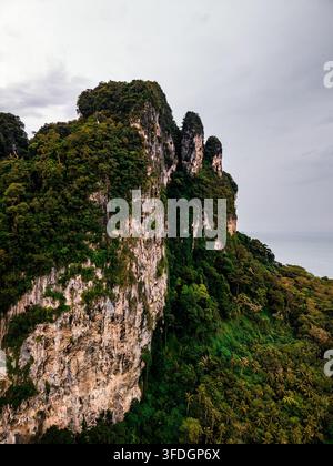 Luftaufnahme einer steilen Kalksteinklippe, die mit üppiger tropischer Vegetation bedeckt ist und sich über das dichte Waldlaub in Ao Nang, Krabi, Thailand erhebt. Stockfoto