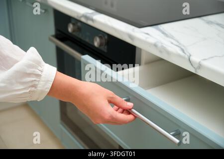 Nahaufnahme einer Person, die eine hellblaue Küchenschublade mit einer Marmorarbeitsplatte und einem eingebauten Backofen im Hintergrund öffnet Stockfoto