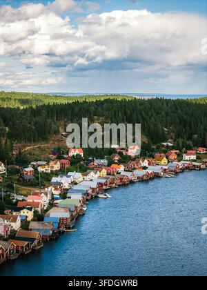Luftaufnahme des historischen Küstendorfs Ulvohamn mit ikonischen roten Holzhäusern, die das Ufer säumen, umgeben von Kiefernwäldern und dem blauen Meer in Stockfoto