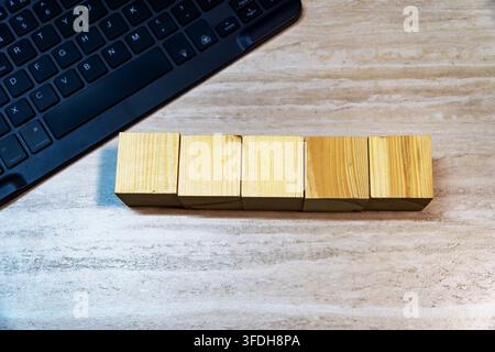 Oberansicht von fünf leeren Holzwürfeln in einer Reihe neben einer schwarzen Computertastatur auf einem Holzschreibtisch. Kopierraum für Text oder Mockup. Stockfoto