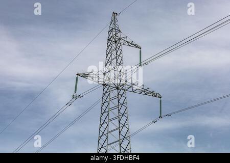 Stahlgitter-Strommast, der Hochspannungsleitungen gegen einen leicht bewölkten blauen Himmel trägt. Stockfoto