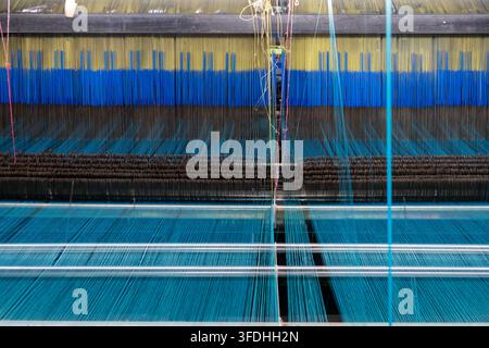 Nahaufnahme einer komplexen angetriebenen Webmaschine mit mehreren farbigen Fäden in Bewegung, die den Prozess der Stoffherstellung in einer Sari-Webfabrik zeigt Stockfoto