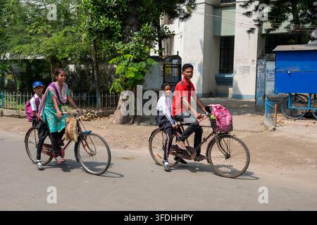Eltern und ihre Kinder fahren mit dem Fahrrad auf einer Straße in Indien, wobei die Kinder hinter ihren Eltern auf demselben Fahrrad sitzen Stockfoto