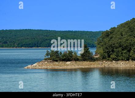 Waldreicher Stauseeufer und felsige Landspitze unter einem klaren blauen Himmel Stockfoto