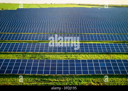 Luftaufnahme einer großen Solarfarm mit Reihen von Photovoltaik-Paneelen über grüne Felder, erneuerbare Energieproduktion, nachhaltige Strominfrastruktur in der ländlichen Landschaft Stockfoto