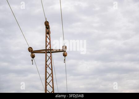 Rostiger Gittermast für die Stromübertragung mit Keramikisolatoren, hängenden Leitern und elektrischer Hardware vor einem weiten grauen Überzugshimmel Stockfoto