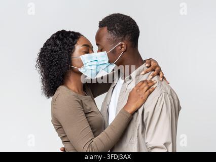 Romantisches afrikanisches Paar in Gesichtsmasken küssen über grau Stockfoto