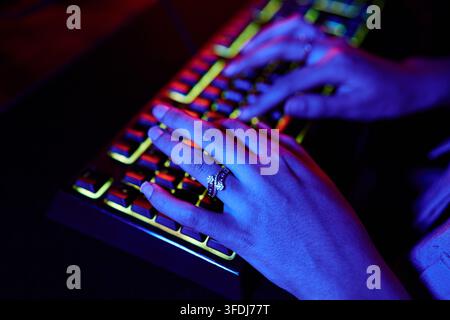 Hackerhände, die auf einer neonbeleuchteten Gaming- oder Codiertastatur in einem dunklen Raum tippen, veranschaulichen Cybersicherheit und Technologie Stockfoto