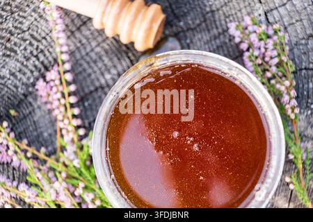 Oberblick auf dunklen bernsteinfarbenen Heidehonig in einem Gläsernen Glas, umgeben von blühender Calluna vulgaris. Natürliches Bienenprodukt und rustikales Bio-Lebensmittelkonzept. Stockfoto