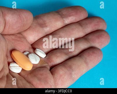 Nahaufnahme einer erwachsenen Hand, die verschiedene Pillen und Tabletten vor einem blauen Hintergrund hält, illustriert Medikamente, Dosierung, Gesundheitswesen, Apotheke, Altern Stockfoto