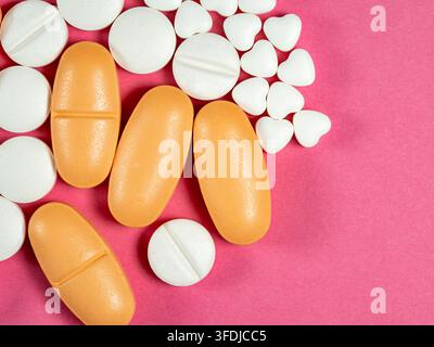 Helle orangefarbene längliche Pillen und weiße runde und herzförmige Tabletten, die auf einem rosa Hintergrund angeordnet sind, vermitteln Medikamente, Apotheke, Gesundheitswesen, Liebe und Stockfoto