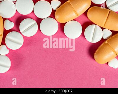 Verschiedene weiße Tabletten und orangefarbene Kapseln, die auf einem lebhaften rosa Hintergrund verstreut sind, einschließlich kleiner herzförmiger Pillen, die Themen der Gesundheit und Fürsorge vermitteln Stockfoto