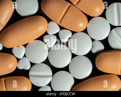 Nahaufnahme von orangefarbenen länglichen und weißen runden Pillen mit kleinen herzförmigen Tabletten auf schwarzem Hintergrund, die Medizin, Gesundheitswesen, Verschreibung anregen Stockfoto