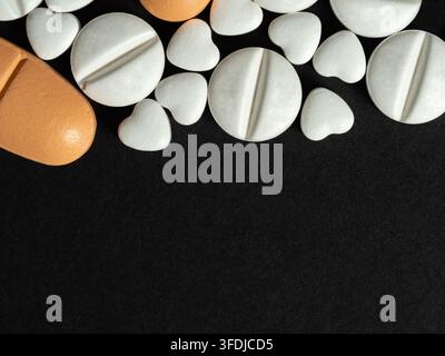 Verschiedene weiße herzförmige und runde Pillen neben orangefarbenen Tabletten auf einem schwarzen Hintergrund, die Medikamente, Herzgesundheit, Apotheke und Vorsorge vermitteln Stockfoto