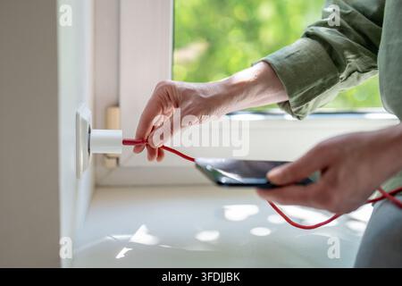 Frau biegt ein defektes USB-Kabel in der Nähe des Wandadapters, um das instabile Laden des Smartphones zu Hause wiederherzustellen. Stockfoto