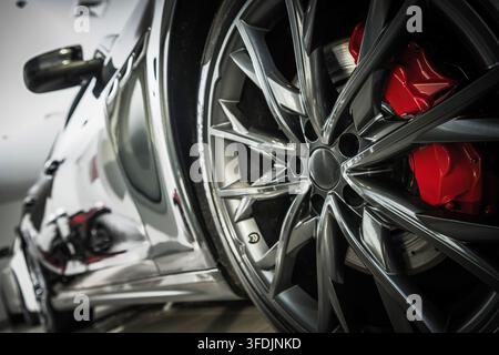 Eine nahe Niedrigwinkelaufnahme hebt ein mehrspeichiges Aluminiumrad, Reifen und Bremssattel hervor. Die polierte Karosserie spiegelt die Inneneinrichtung wider. Stockfoto