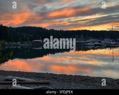 Lebendiger orangefarbener Sonnenuntergang über ruhigen Meereswellen, der warme Himmel farben bei der Marina in Heriot Bay, Quadra Island, British Columbia, Kanada widerspiegelt Stockfoto