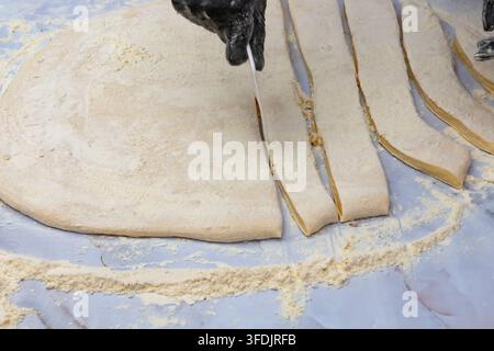 Lange Streifen rohen Teigs, die auf einem mit Mehl bedeckten Arbeitstisch angeordnet sind Stockfoto