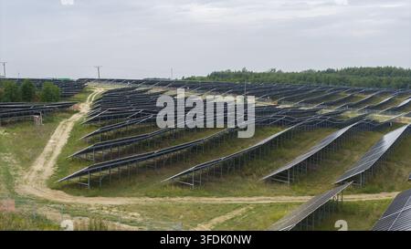 Luftaufnahme einer großen Solarfarm im Bau mit Reihen von Photovoltaikmodulen, die auf Metallrahmen montiert sind, Schotterzugängen und grasbewachsenem Gelände Stockfoto