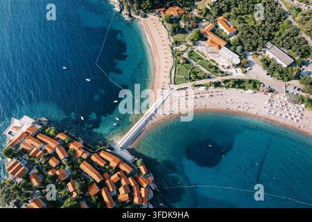 Ein atemberaubendes Luftbild fängt das ikonische Aman Hotel auf der Insel Sveti Stefan, Montenegro, ein und zeigt die schmale Landenge, die die historische Insel mit dem Festland verbindet, sandige Strände, die türkise Adria und das üppige Grün, das das Resort umgibt Stockfoto