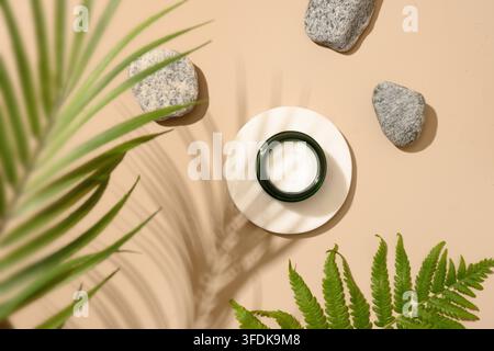 Podium für Kosmetikprodukte in moderner Komposition mit tropischen Farnblättern und Steinen auf beigem Hintergrund mit Schatten. Blick von oben. Stockfoto