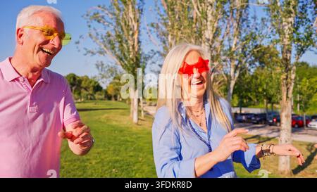 Fröhliches Seniorenehepaar lacht und tanzt zusammen in einem Park Stockfoto