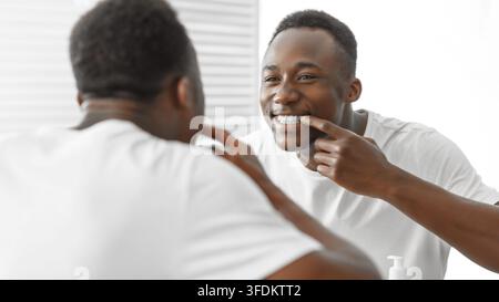 Afrikanischer Mann Überprüft Zähne Lächelnd Im Spiegel Stehend Im Badezimmer Stockfoto