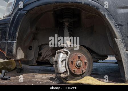 Nahaufnahme eines freiliegenden Autobremssystems ohne Rad auf einer schmutzigen Reparaturplattform. Stockfoto