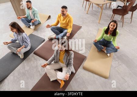 Arbeitsplatz-Wohlbefinden und Stressmanagement, vielfältige Mitarbeiter praktizieren Meditation und Achtsamkeit auf Yogamatten in einem modernen Büro während einer Pause Stockfoto