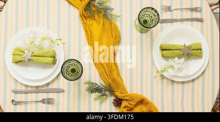 Tischgedeck für das Abendessen, Gastfreundschaft und Essen mit gelbem Läufer und grünen Servietten auf gestreiftem Tischtuch für festliche Heimveranstaltung oder Party Stockfoto