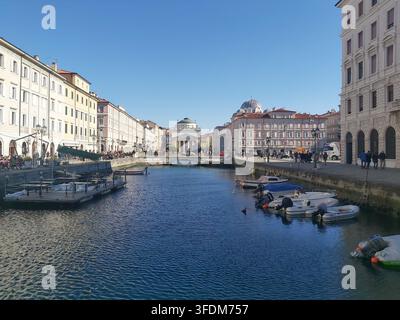 Blick auf den Triest Canal Grande Wasserweg in Richtung der neoklassizistischen Fassade der Sant Antonio Taumaturgo-Kirche mit festgemachten Booten an einem sonnigen Tag in Italien Stockfoto