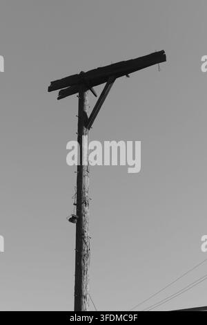 Hoher hölzerner Strommast vor klarem blauem Himmel. Der Mast zeigt eine verwitterte Textur und verrostete Metallbügel. Bild geeignet für Bau, ländliche Gebiete oder in Stockfoto