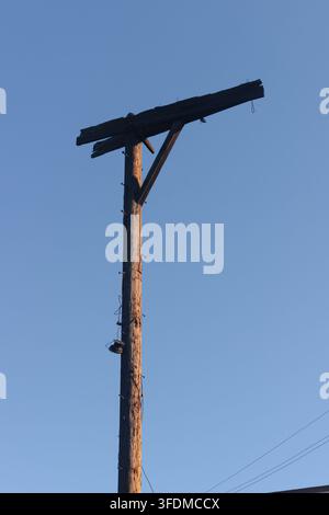 Hoher hölzerner Strommast vor klarem blauem Himmel. Der Mast zeigt eine verwitterte Textur und verrostete Metallbügel. Bild geeignet für Bau, ländliche Gebiete oder in Stockfoto