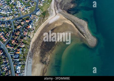 Luftbild von oben über den Penrhyn Bay Beach, das geschwungene Gezeiten-Sände, klares grünes Küstenwasser, Wohnhäuser, Straßen und einen langen Stein-Promenade zeigt Stockfoto