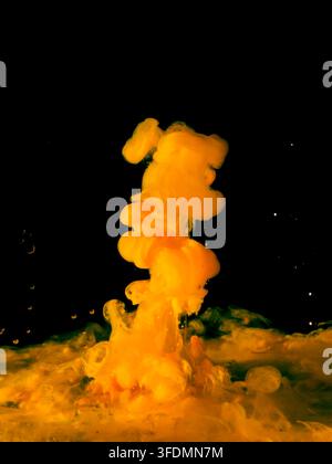 Eine lebhafte gelbe Tintenwolke zerstreut sich und wirbelt im Wasser vor einem tiefschwarzen Hintergrund und zeigt flüssige Bewegung und lebendigen Farbkontrast. Stockfoto