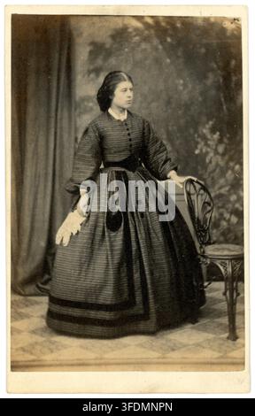 Vintage-Foto 1860er Jahre, viktorianische attraktive junge Frau, trägt ein kariertes Kleid im Crinoline-Stil, hält ein weißes Spitzenhöschen, datiert auf den 18. November 1861, UK Stockfoto