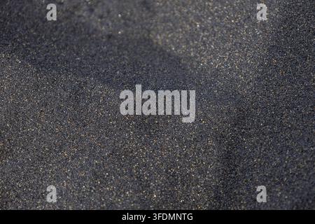 Dunkler schwarzer Sand, der natürliches Glitzern und eine feinkörnige Textur zeigt Stockfoto