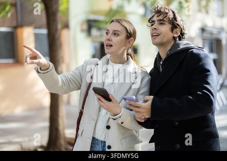 Ein junges Paar, das auf der Straße läuft und sich die Handys für die Stadtkarte ansieht Stockfoto