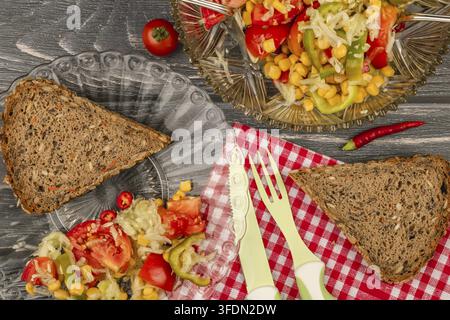 Salatteller mit einer Scheibe braunem Brot und frischem Gemüse auf einem rustikalen Holztisch mit karierter Tischdecke Stockfoto
