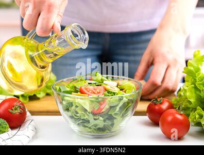 Frauenhände gießen Olivenöl in den Gemüsesalat. Nahaufnahme. Selektiver Fokus. Stockfoto