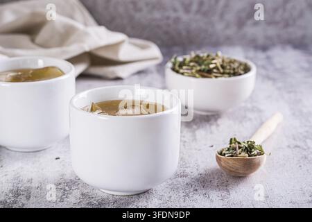 Kalter grüner japanischer Hojicha-Tee mit Eis in Tassen und loser Tee in einer Schale auf dem Tisch Stockfoto