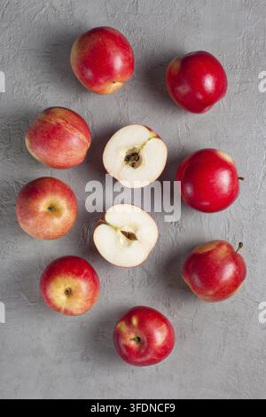 Viele rote reife Äpfel auf einem grauen Hintergrund, einer in der Mitte geschnitten, von oben aufgenommen. Hintergrunddesign mit frischen roten Äpfeln. Erntekonzept. P Stockfoto