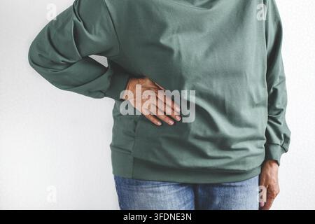 Nahaufnahme der älteren Frau in grünem Hoodie und Jeans, die ihre Seite halten, leiden an Flanke oder Bauchschmerzen auf weißem Hintergrund, Konzept Gesundheit Stockfoto