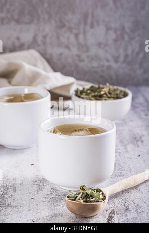 Kalter grüner japanischer Hojicha-Tee mit Eis in Tassen und trockener Tee in einer Schüssel auf dem Tisch. Vertikale Ansicht Stockfoto