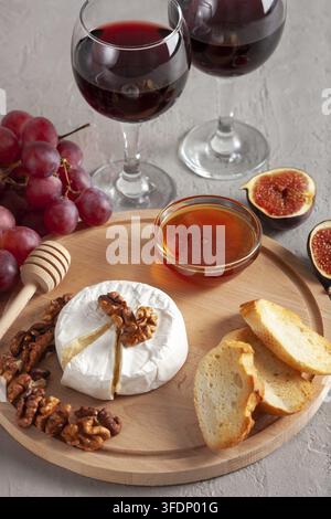 Käseplatte, Stillleben von saisonalen Weinsnacks. Camembert- oder Brie-Käse mit Gläsern Rotwein, Trauben, Walnüssen, Baguette, Honig und Feigen. Käse Stockfoto