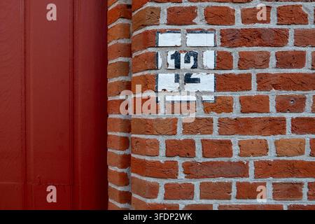 Nahaufnahme einer verwitterten Hausnummer, die auf eine alte rote Ziegelwand neben einer tiefroten Holztür im historischen Zentrum von Brügge Brugge West Fla gemalt ist Stockfoto