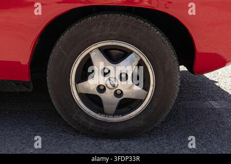 Tavernes Blanques, Spanien – 14. Juni 2026. Ein fünfzackiges Leichtmetallrad wird im Detail gezeigt mit einer blauen Ford-Mittenkappe. Das Rad ist montiert an einem roten Coupé p Stockfoto