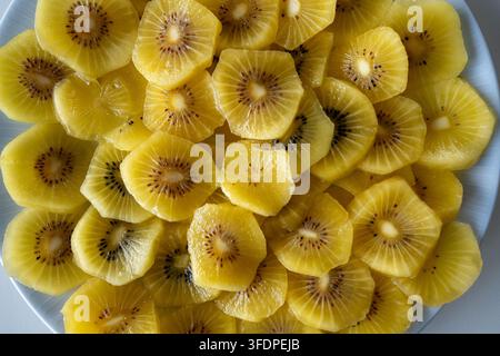 Ansicht von oben über ordentlich angeordnete goldene Kiwischeiben auf einem weißen Teller, die hellgelbes Fruchtfleisch, feine Samen und saftige Textur für gesundes Brei zeigen Stockfoto