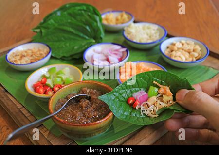 Nahaufnahme einer Männerhand, die ein traditionelles thailändisches Vorspeisen-Miang-Kham-Wrap mit bunten Zutaten hält, bevor es gegessen wird Stockfoto