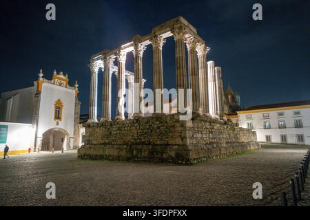 Alte römische Tempelruinen in Évora, Portugal, die nachts dramatisch beleuchtet sind und hohe korinthische Säulen, Steinfundamente und die umgebende historische Umgebung zeigen Stockfoto